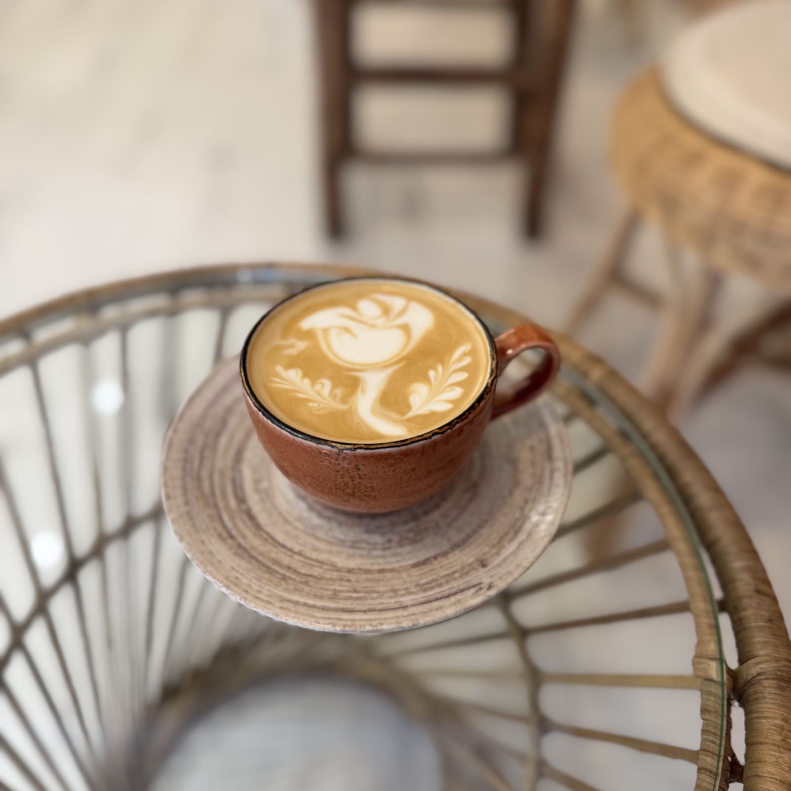 A cappuccino in a terracotta cup with leaf latte art on a stoneware saucer