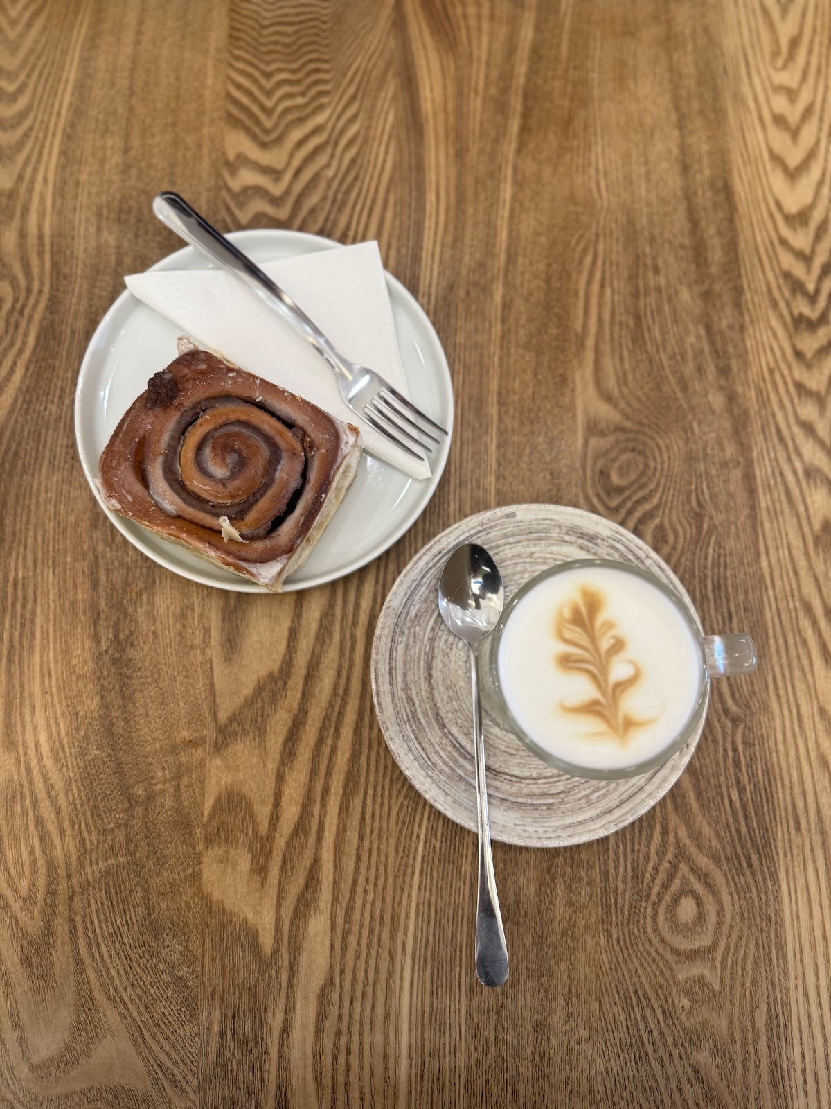 A cinnamon roll on a plate beside a flat white with feather latte art