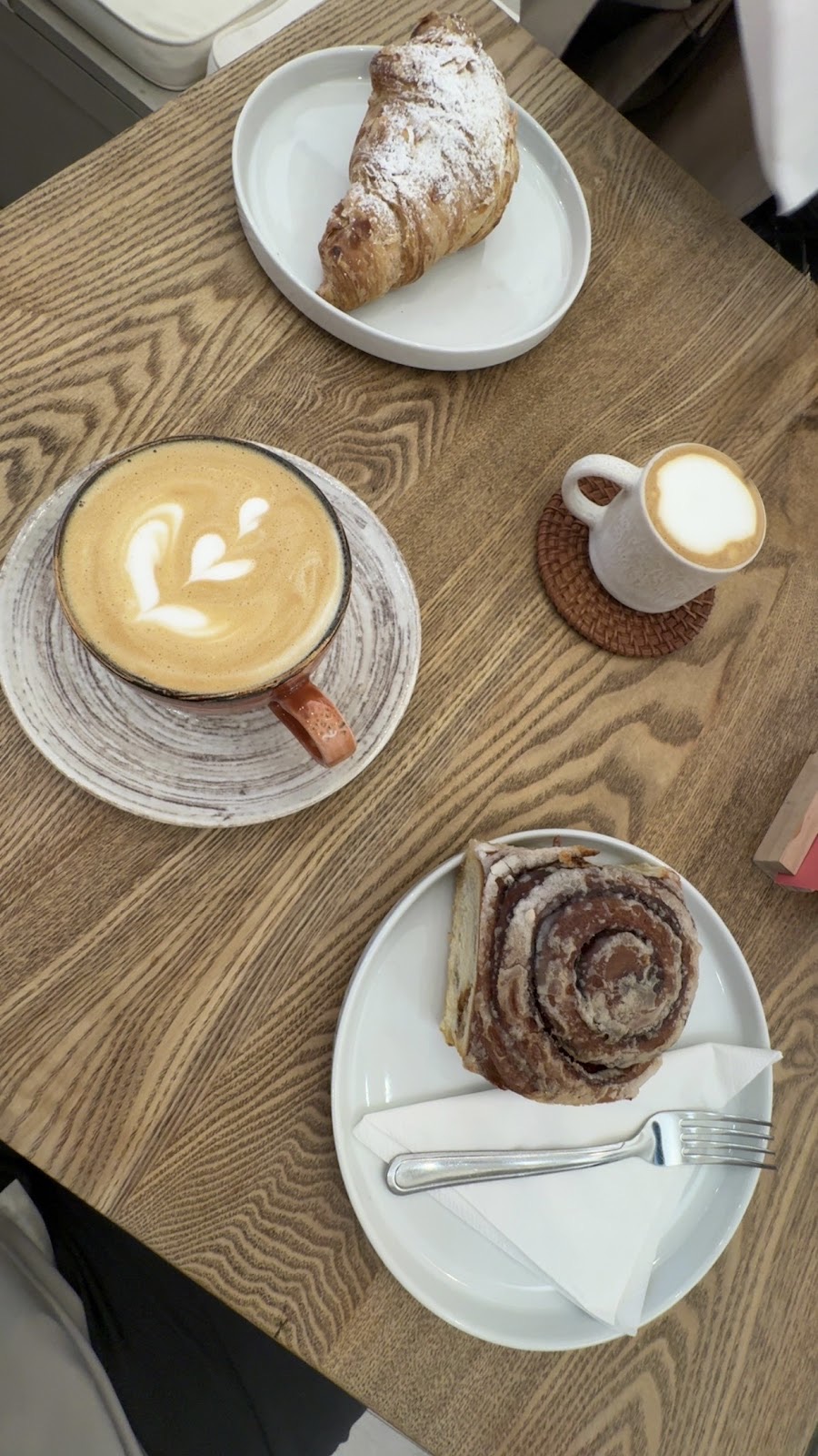 An overhead spread of a croissant, a latte, a milk jug and a cinnamon bun