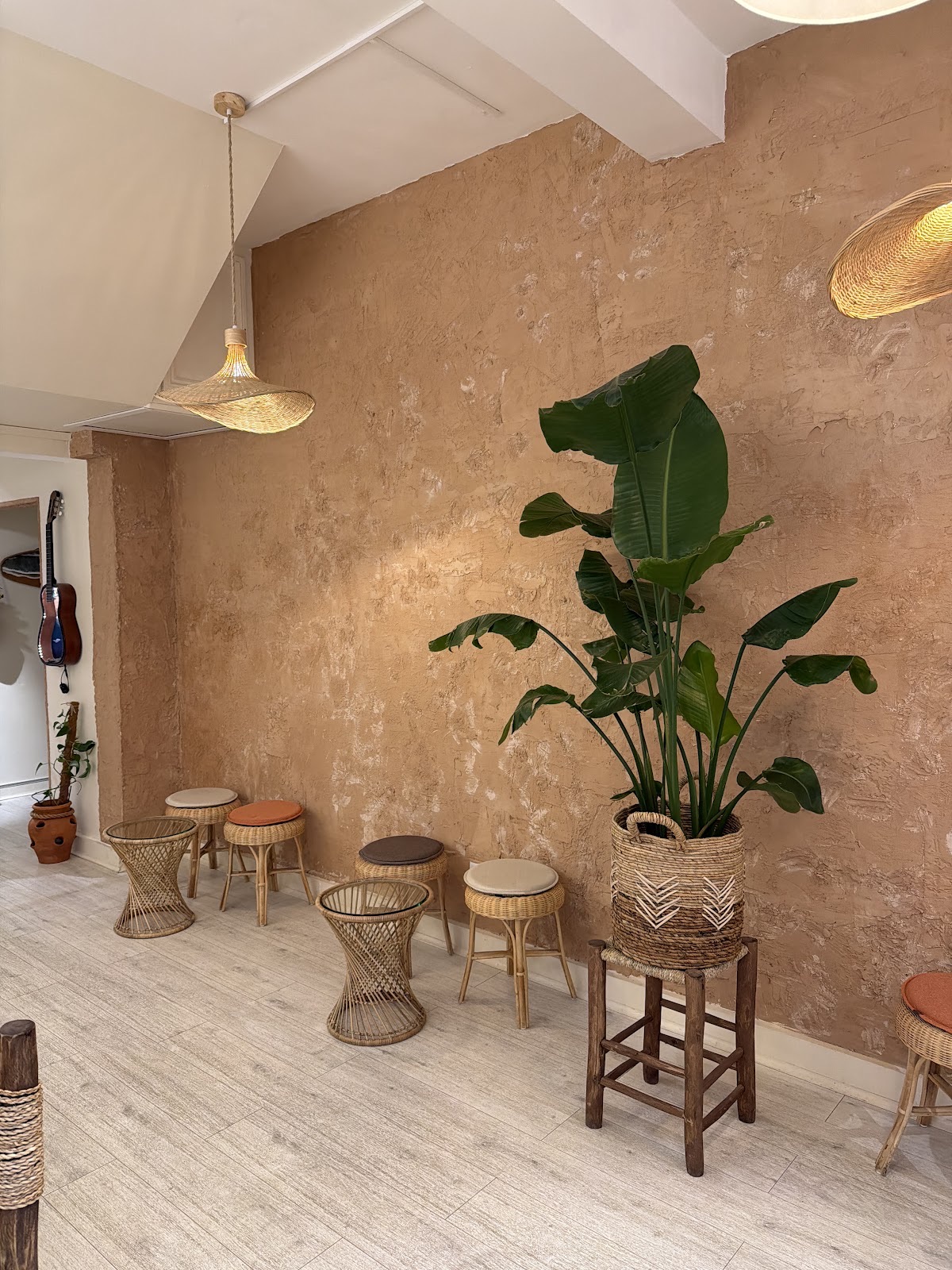 A corner of the seating area with a terracotta plaster wall, a large plant and woven stools under rattan pendants